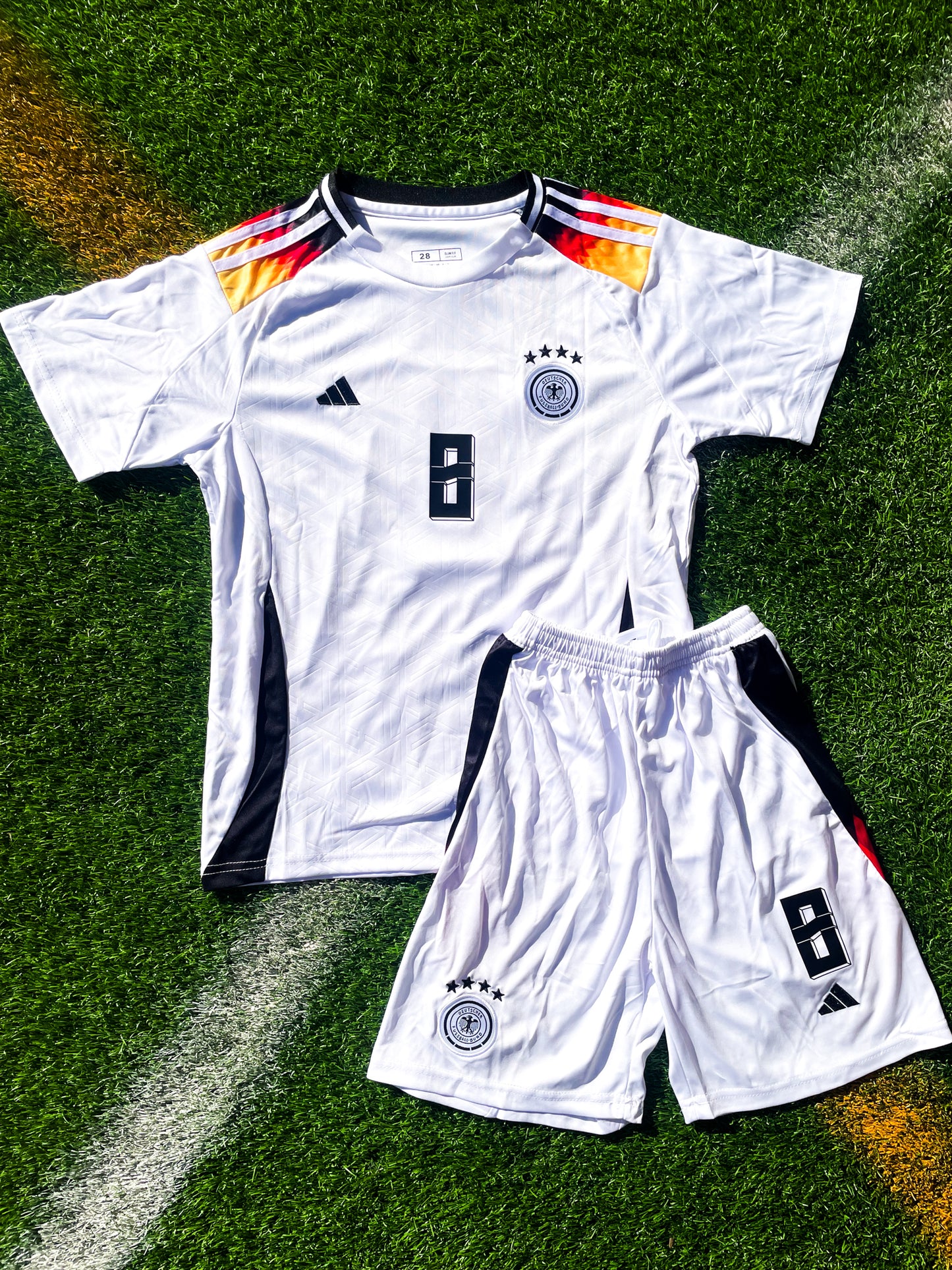 Front of Germany 2024 kids home jersey with black shoulders and gradient trim