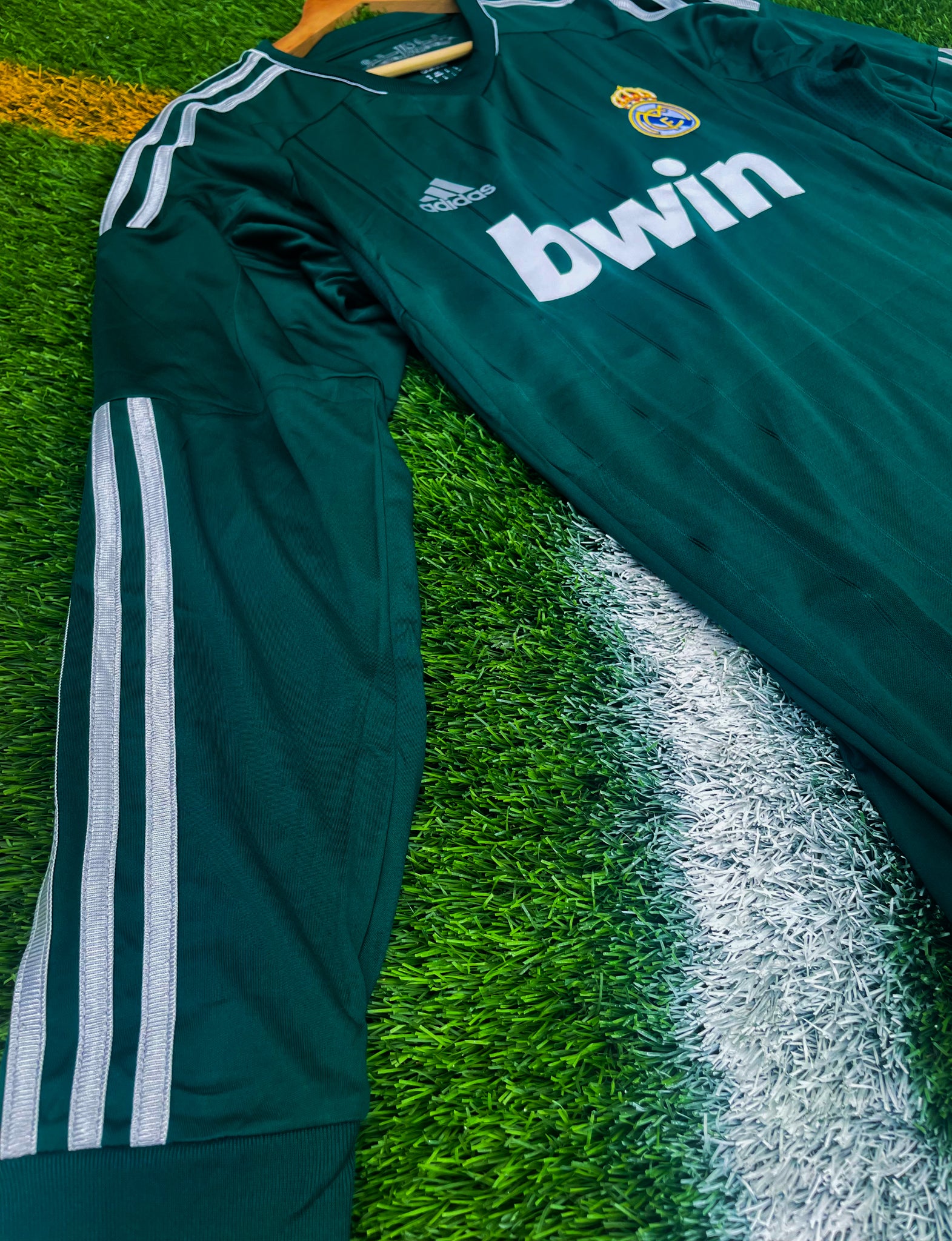 Close-up of embroidered club crest and Adidas stripes on green fabric

